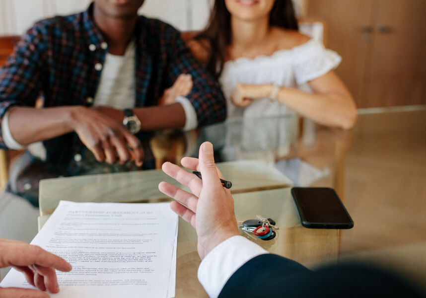 Home buyers at table with agent. House keys and contract on the table.